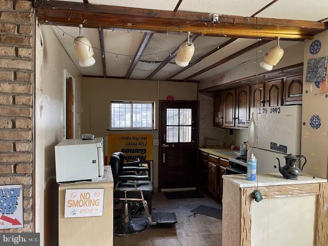 interior space featuring hanging light fixtures, dark brown cabinets, white refrigerator, brick wall, and dark tile floors