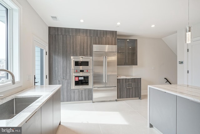 kitchen with appliances with stainless steel finishes, light tile patterned floors, light stone countertops, hanging light fixtures, and sink