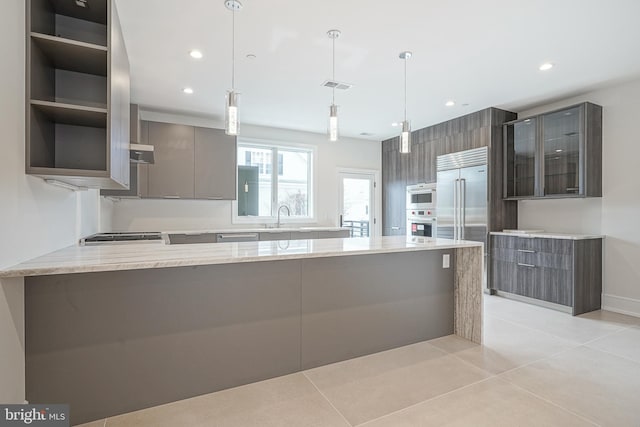 kitchen with sink, light stone counters, kitchen peninsula, light tile patterned floors, and decorative light fixtures