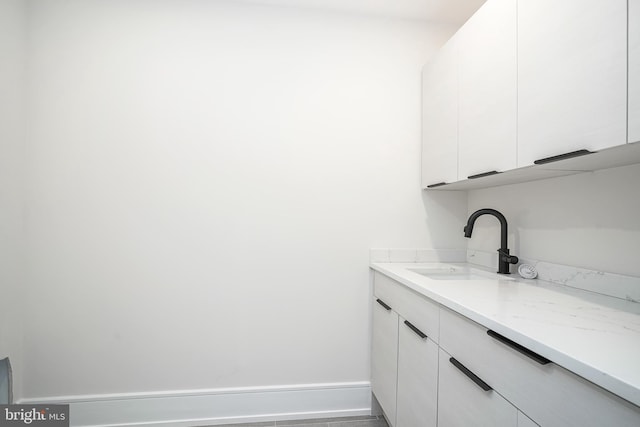 bar with white cabinets, sink, and light stone counters