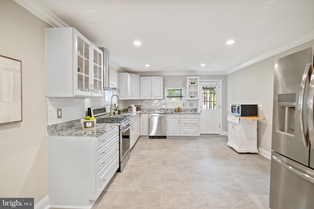 kitchen featuring white cabinetry, appliances with stainless steel finishes, wall chimney range hood, ornamental molding, and light stone counters