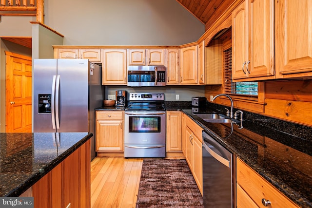 kitchen with sink, dark stone countertops, stainless steel appliances, high vaulted ceiling, and light wood-type flooring