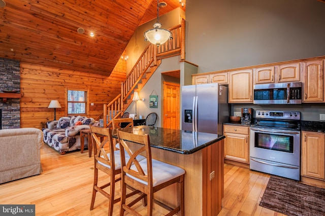 kitchen with wood walls, a breakfast bar area, stainless steel appliances, light wood-type flooring, and high vaulted ceiling