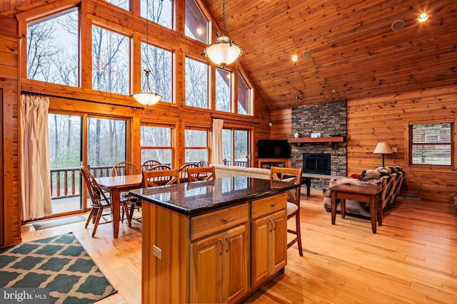 kitchen with wooden walls, decorative light fixtures, a stone fireplace, high vaulted ceiling, and light hardwood / wood-style flooring