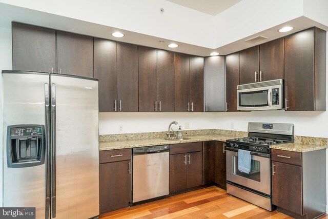 kitchen with light hardwood / wood-style floors, stainless steel appliances, sink, and light stone countertops