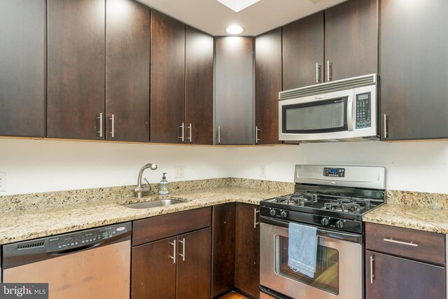 kitchen featuring appliances with stainless steel finishes, dark brown cabinetry, sink, and light stone countertops