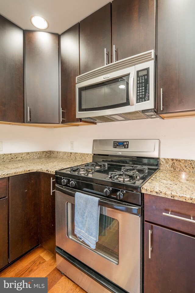 kitchen featuring gas stove, light hardwood / wood-style flooring, dark brown cabinets, and light stone counters