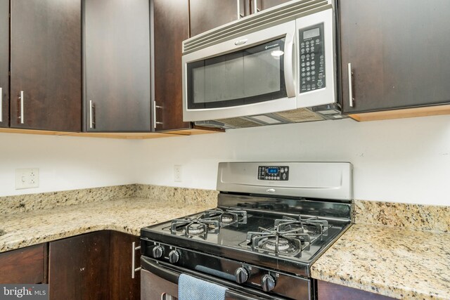 kitchen featuring light stone countertops, gas range oven, and dark brown cabinetry