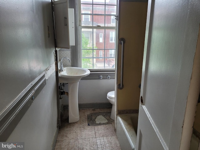 bathroom with tile patterned flooring, a tub to relax in, and toilet