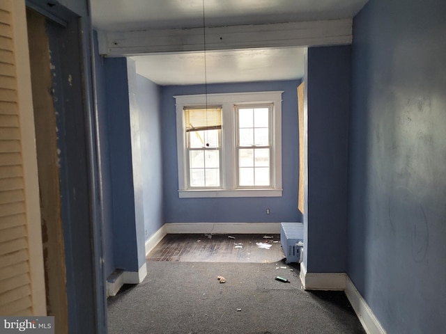 unfurnished dining area featuring dark colored carpet and beamed ceiling