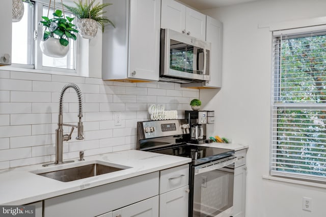 kitchen with appliances with stainless steel finishes, sink, plenty of natural light, and white cabinets