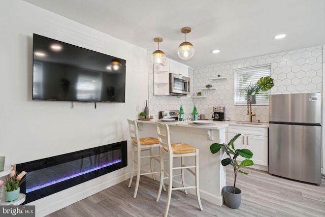 kitchen with hanging light fixtures, white cabinetry, appliances with stainless steel finishes, light wood-type flooring, and tasteful backsplash