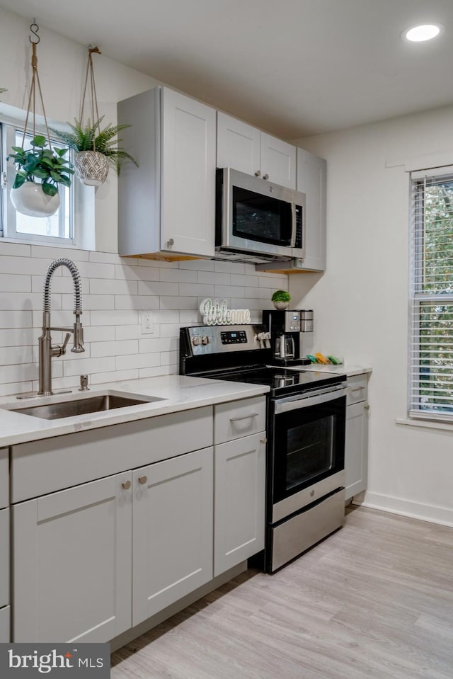 kitchen with appliances with stainless steel finishes, pendant lighting, sink, and light wood-type flooring