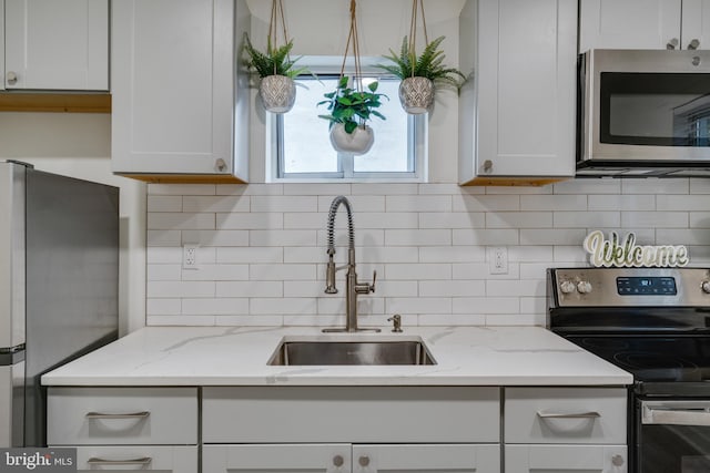 kitchen with appliances with stainless steel finishes, tasteful backsplash, light stone counters, sink, and white cabinetry