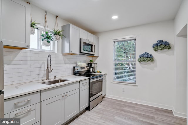 kitchen featuring appliances with stainless steel finishes, backsplash, light hardwood / wood-style floors, sink, and light stone countertops