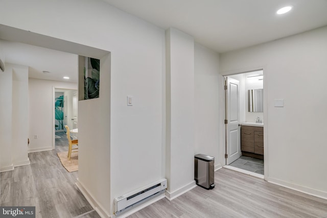 corridor with sink, light wood-type flooring, and a baseboard heating unit