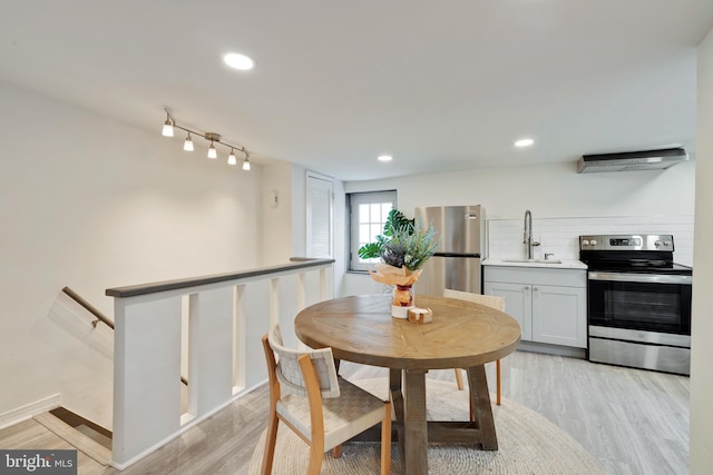 dining room featuring rail lighting, sink, and light hardwood / wood-style flooring