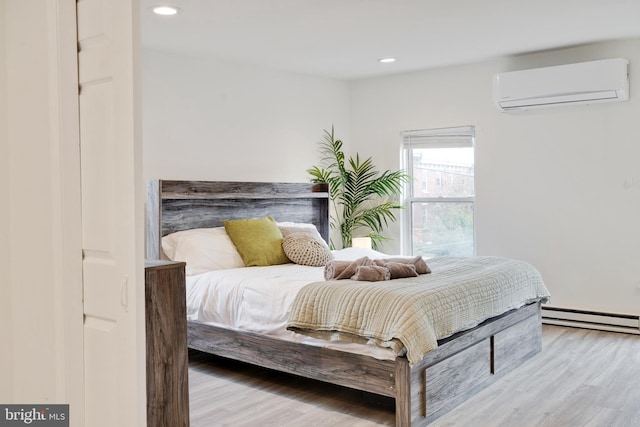 bedroom featuring a wall unit AC, baseboard heating, and light hardwood / wood-style flooring