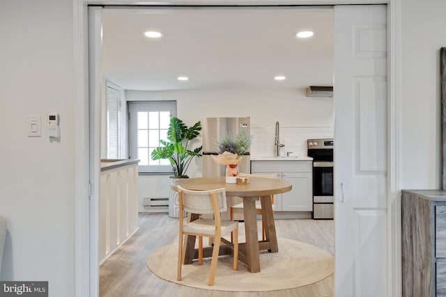 dining area with light hardwood / wood-style floors, a baseboard heating unit, and sink