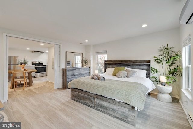 bedroom with an AC wall unit, light hardwood / wood-style flooring, and stainless steel refrigerator