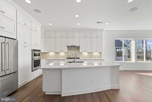 kitchen with a kitchen island with sink, sink, dark hardwood / wood-style floors, white cabinetry, and stainless steel appliances