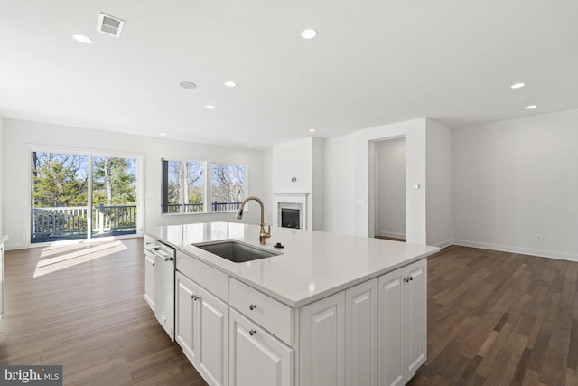 kitchen featuring a kitchen island with sink, sink, stainless steel dishwasher, dark hardwood / wood-style flooring, and white cabinetry