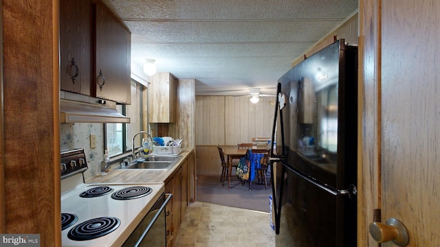 kitchen featuring black refrigerator, sink, electric range, and wooden walls