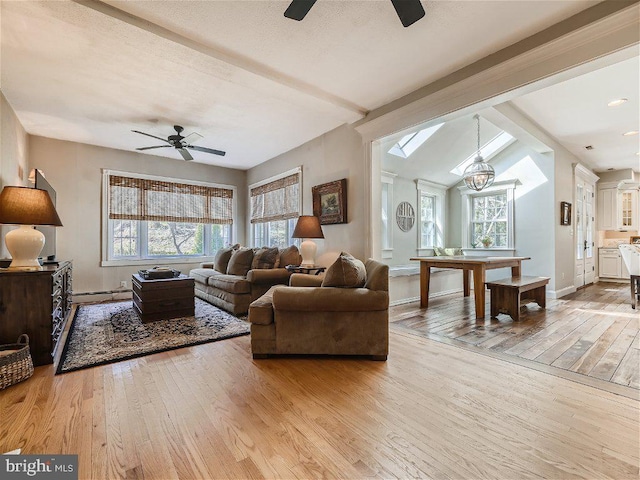 living room with light hardwood / wood-style floors, a baseboard radiator, lofted ceiling with beams, and ceiling fan with notable chandelier