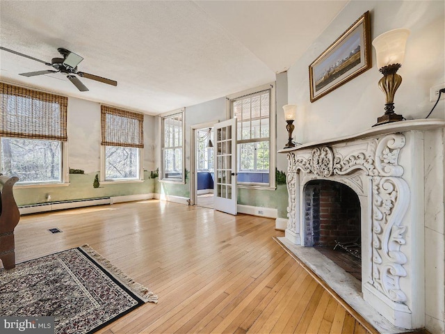 living room featuring ceiling fan, a high end fireplace, a baseboard heating unit, light hardwood / wood-style flooring, and french doors