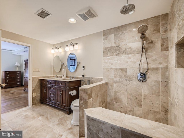 bathroom with toilet, vanity, tiled shower, tile walls, and tile flooring