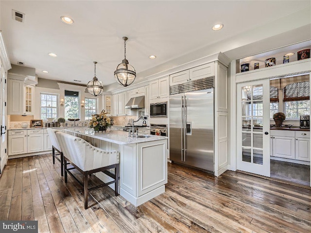 kitchen featuring a breakfast bar, decorative light fixtures, dark hardwood / wood-style flooring, built in appliances, and white cabinetry