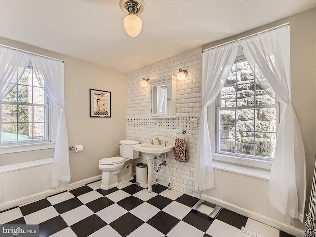 bathroom with toilet, tile walls, tile flooring, and sink