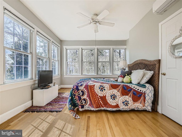 bedroom with ceiling fan, an AC wall unit, and light hardwood / wood-style floors