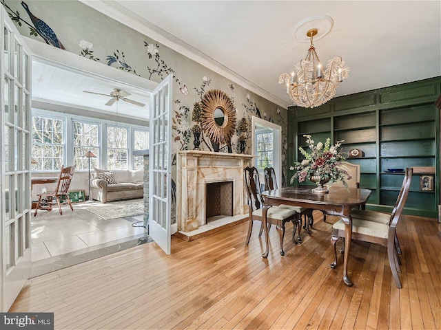 dining area featuring a high end fireplace, ornamental molding, light wood-type flooring, and ceiling fan with notable chandelier