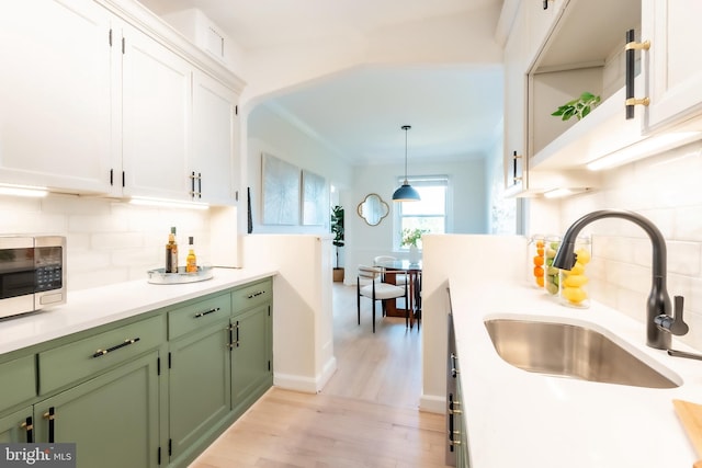 kitchen with white cabinetry, tasteful backsplash, hanging light fixtures, green cabinetry, and sink