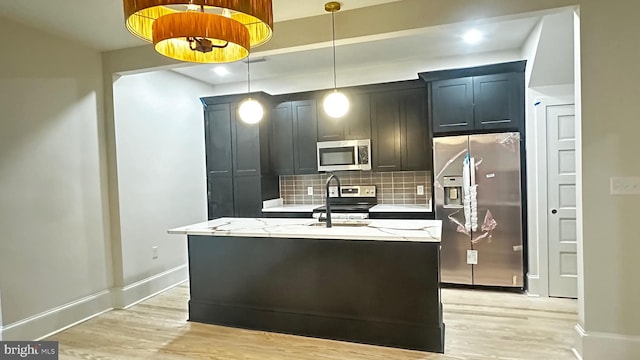 kitchen with light stone counters, hanging light fixtures, tasteful backsplash, light hardwood / wood-style flooring, and stainless steel appliances