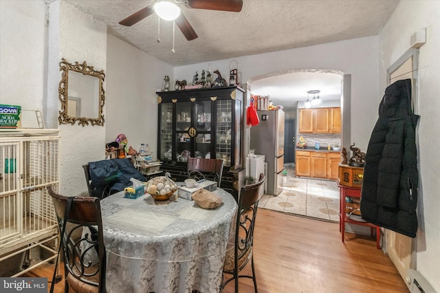 dining space featuring light tile floors, ceiling fan, a textured ceiling, and a baseboard heating unit