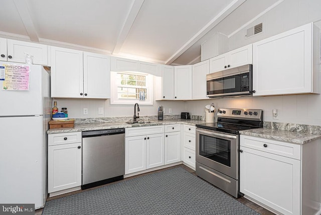 kitchen featuring appliances with stainless steel finishes, sink, vaulted ceiling with beams, white cabinetry, and light stone countertops