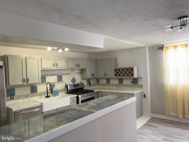 kitchen with backsplash, sink, light wood-type flooring, a textured ceiling, and stainless steel appliances