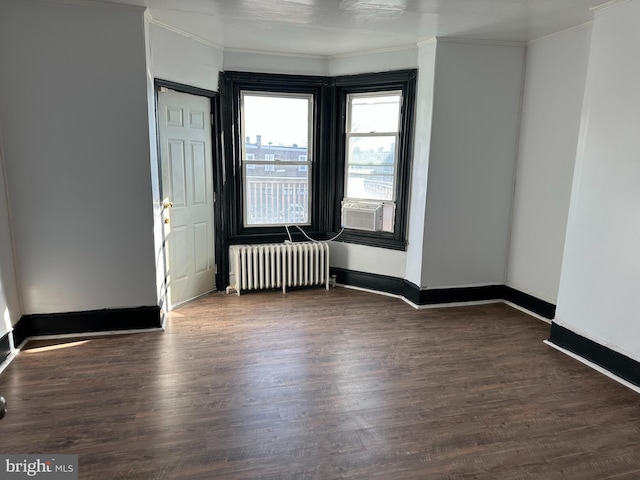 empty room with dark hardwood / wood-style floors, ornamental molding, and radiator