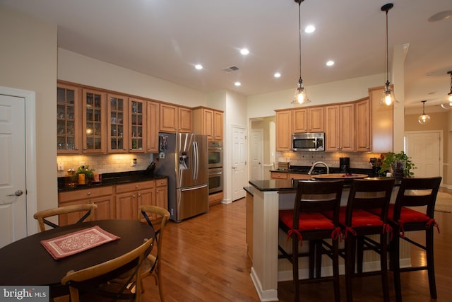 kitchen with decorative light fixtures, backsplash, dark wood-type flooring, a breakfast bar, and appliances with stainless steel finishes