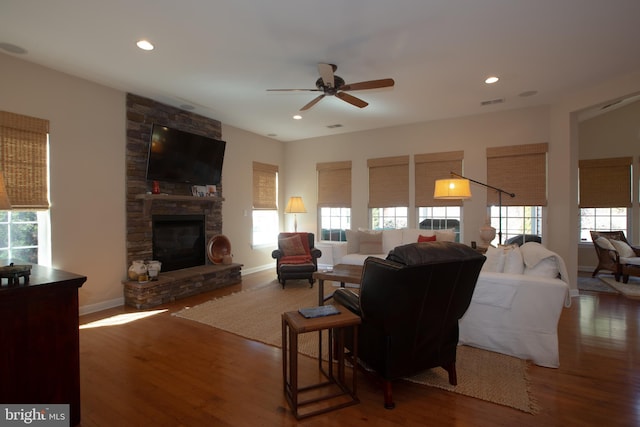 living room featuring dark hardwood / wood-style flooring, ceiling fan, and a stone fireplace