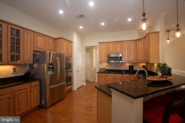 kitchen with appliances with stainless steel finishes, dark stone countertops, light hardwood / wood-style flooring, backsplash, and a breakfast bar area