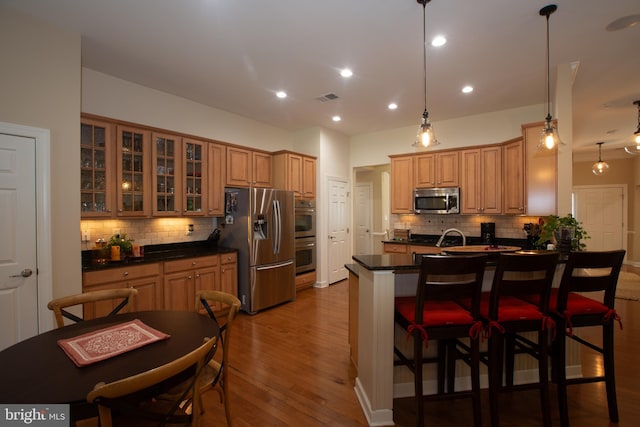 kitchen with appliances with stainless steel finishes, tasteful backsplash, a breakfast bar, decorative light fixtures, and dark hardwood / wood-style floors