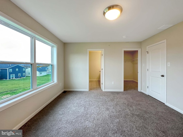 unfurnished bedroom with a spacious closet, a closet, and carpet