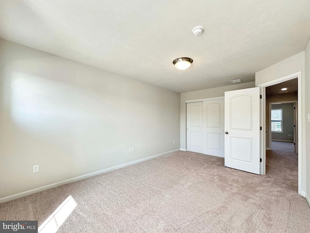 unfurnished bedroom featuring a textured ceiling, light colored carpet, and a closet