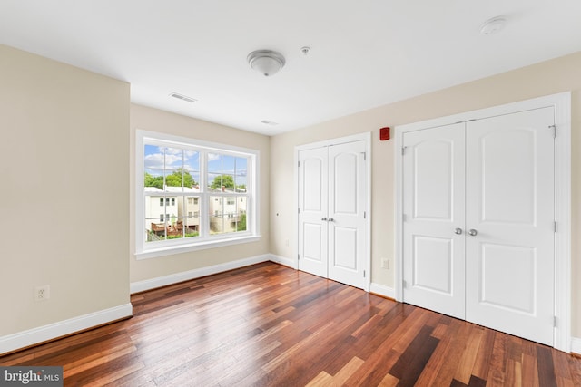 unfurnished bedroom featuring multiple closets and dark wood-type flooring