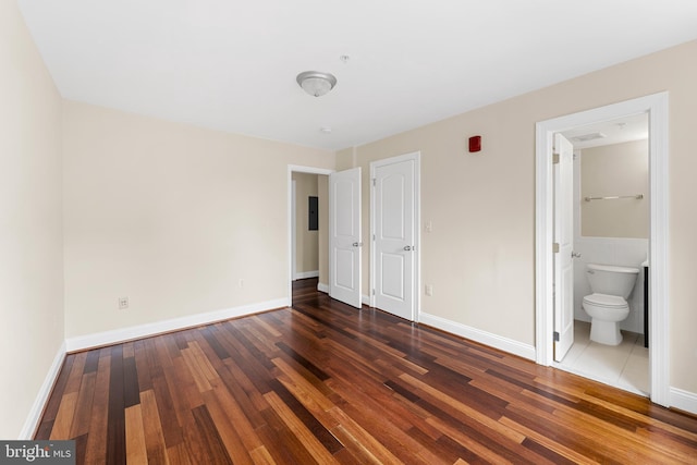 unfurnished bedroom featuring ensuite bath and dark wood-type flooring