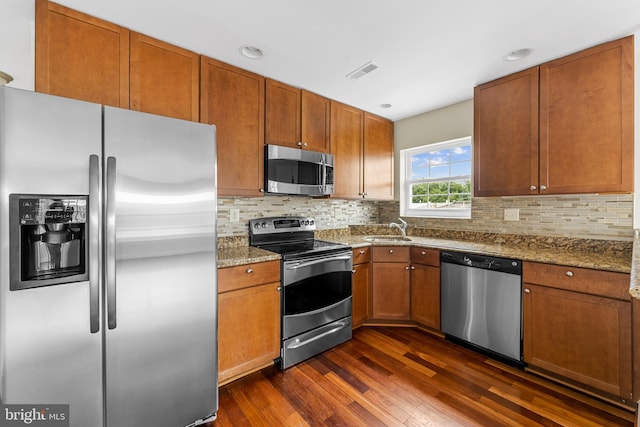 kitchen featuring dark wood-type flooring, appliances with stainless steel finishes, light stone countertops, backsplash, and sink