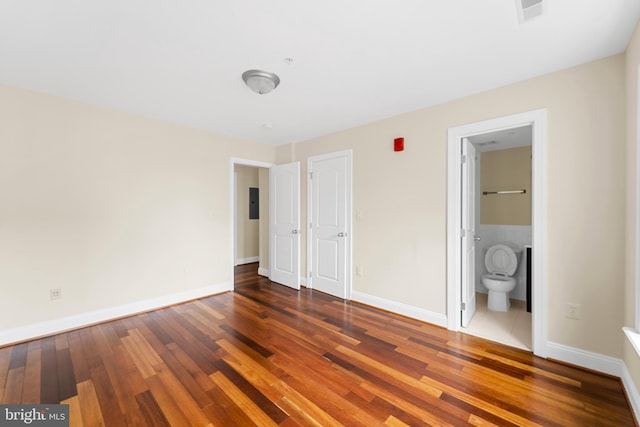 unfurnished bedroom featuring ensuite bath and dark wood-type flooring